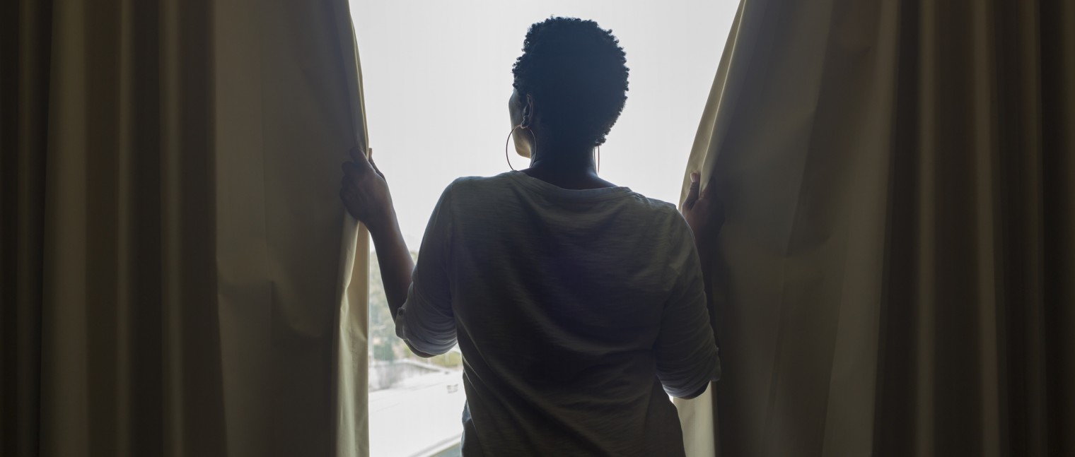 A person opening curtain to expose the sunlight coming through the bedroom windows.