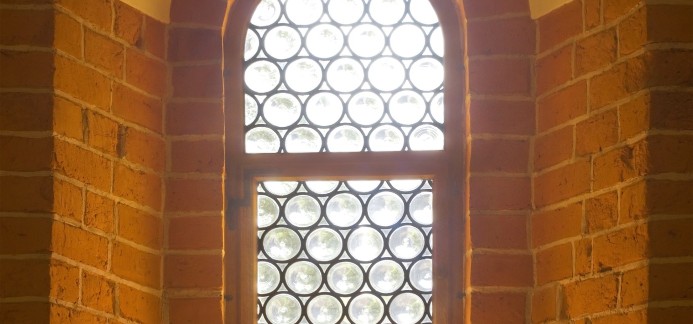 Old church window in sunlight with candles lit in front of the window.