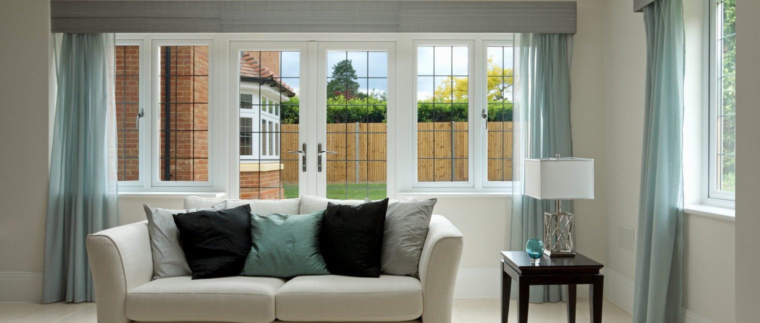 A simple composition of a settee with side table set in a luxury new home. Black silk cushions on the settee complement the dark wood table whilst the  light turquoise cushion and the glass bowl on the table match the curtains. The settee is a light cream colour and sits on a light marble floor.