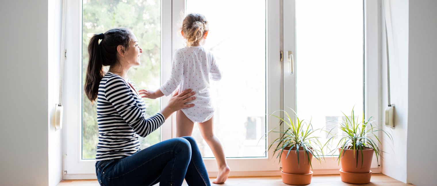 Mother with her little daughter looking out of a bay window.