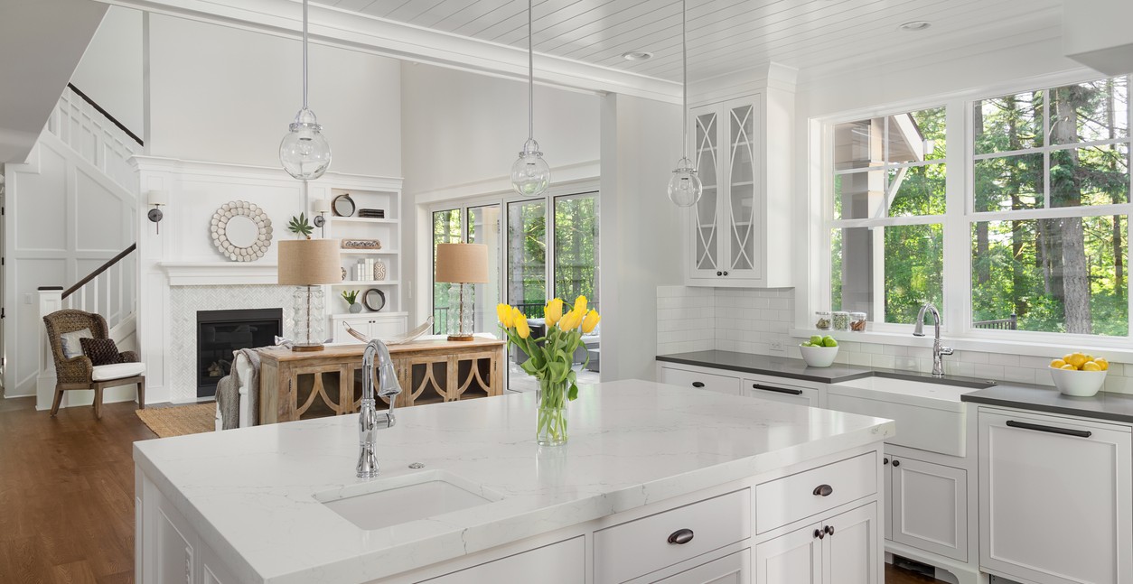 Beautiful kitchen interior with island, two sinks, hardwood floors, and view of living room with vaulted ceilings.