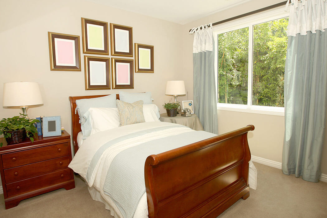 A standard bedroom with a replacement double-slider window with white and grey curtains.