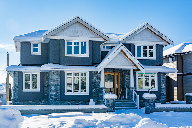 On a winter day, an exterior view of a large brick house with blue siding.