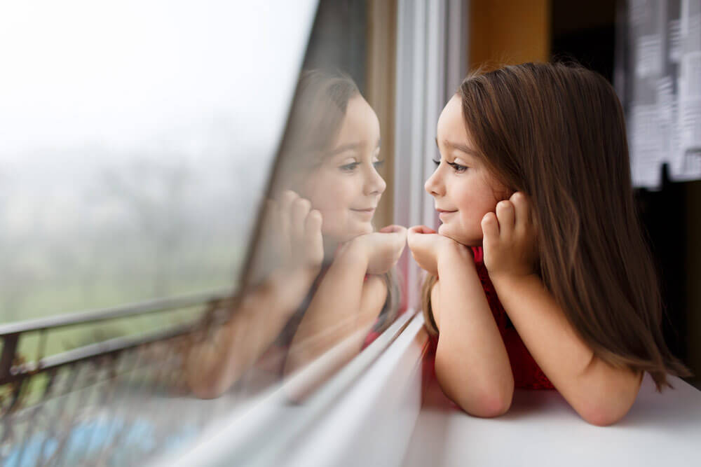 Little girld looking out of a window on an overcast day.